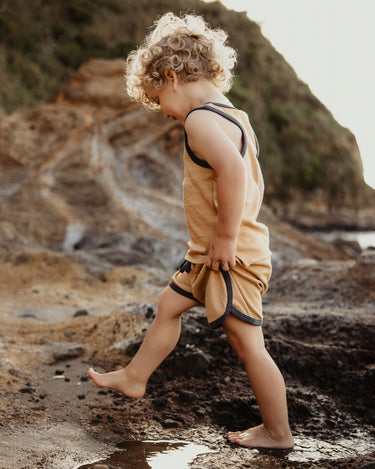 Toddler wearing organic cotton contrast trim shorts exploring beach rocks in marigold yellow – GOTS certified – Babu