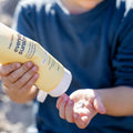 Child holding a tube of sunscreen in a natural setting