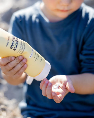 Child holding a tube of sunscreen in a natural setting